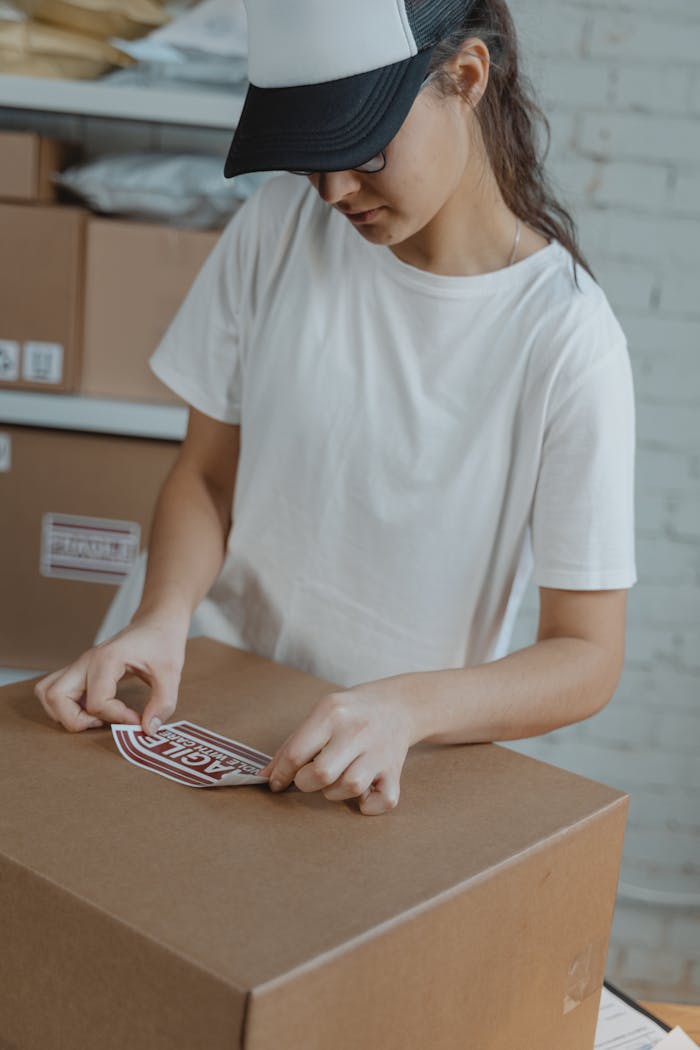 services-02 Woman preparing shipment by applying a 'fragile' sticker on a cardboard box in a warehouse.
